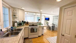 Cocina compacta con pileta, estufa, microondas y comedor con televisión.