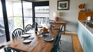 Un comedor con una mesa de madera dispuesta para cuatro personas, sillas, una mesita auxiliar con una lámpara y vistas al exterior a través de una puerta corredera.