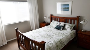 Un dormitorio con cama de madera, una mesita de noche, una ventana con cortinas y un cuadro enmarcado en la pared.