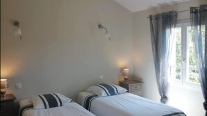 A room with two beds, a window with curtains, and a wooden ceiling beam. - Gîte l'Amandier (Vogüé)
