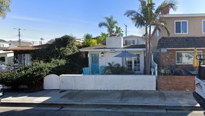 A two-story building with a white exterior, a blue door, and a small patio area with a table and chairs. - Charming Newport Beach Home (Newport Beach)