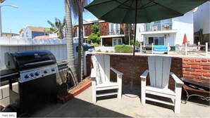 A patio with a grill, two Adirondack chairs, and a large umbrella. - Charming Newport Beach Home (Newport Beach)