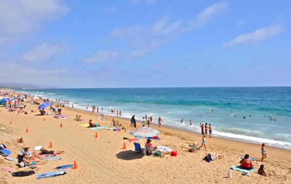 A crowded beach with people sunbathing and swimming, and a clear blue sky.