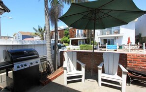 A patio with a grill, two Adirondack chairs, and a large umbrella.