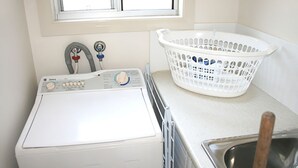Ett kompakt tvättrum med en tvättmaskin med frontmatning, en vit tvättkorg och en diskho i rostfritt stål.