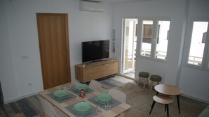 A dining area with a wooden table set for four, a television on a wooden cabinet, and a view of the outside through a glass door. - Central apartment in Moraira (Moraira)