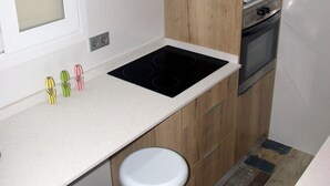A compact kitchen with a white countertop, wooden cabinets, a built-in microwave, and a stove. There are two white bar stools under the counter. - Central apartment in Moraira (Moraira)