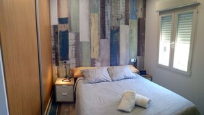 A neatly made bed with a folded towel, a bedside lamp, and a wall with a patchwork design. - Central apartment in Moraira (Moraira)
