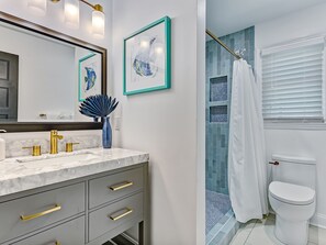 Een badkamer met een wit toilet, een douche met blauwe tegels, een marmeren wastafel met gouden details en kunstwerken in lijsten aan de muur.