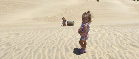 A child playing on a sandy beach with a dune in the background.