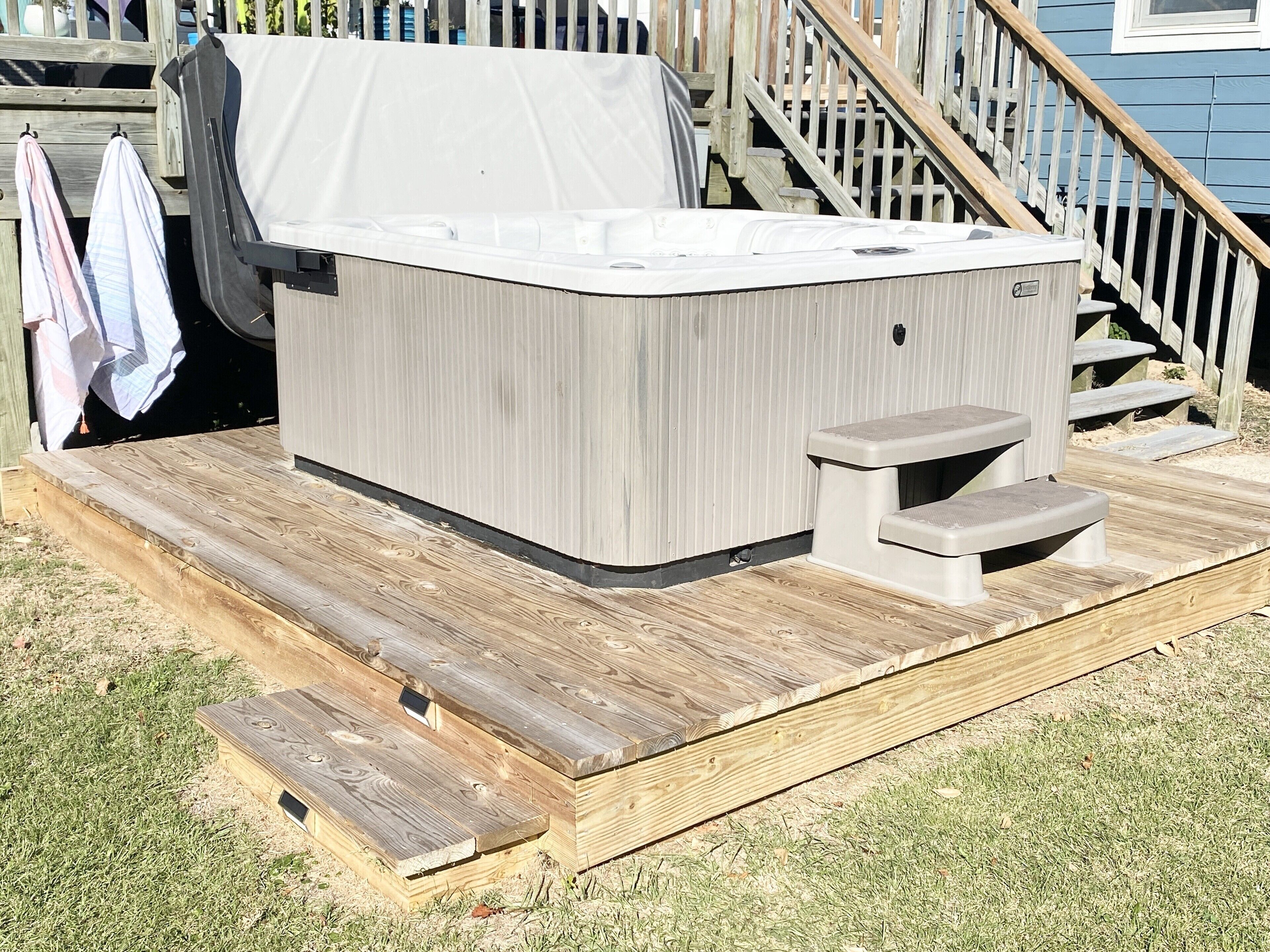 Un jacuzzi con muelle de madera y escalones, rodeado de una valla de madera y una casa al fondo.