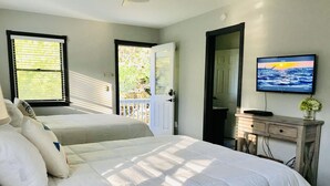 A bedroom with two beds, a TV on a wooden dresser, and a door leading to a balcony. - On Jockey Ridge State Park + Hot Tub & Center of OBX (Nags Head)