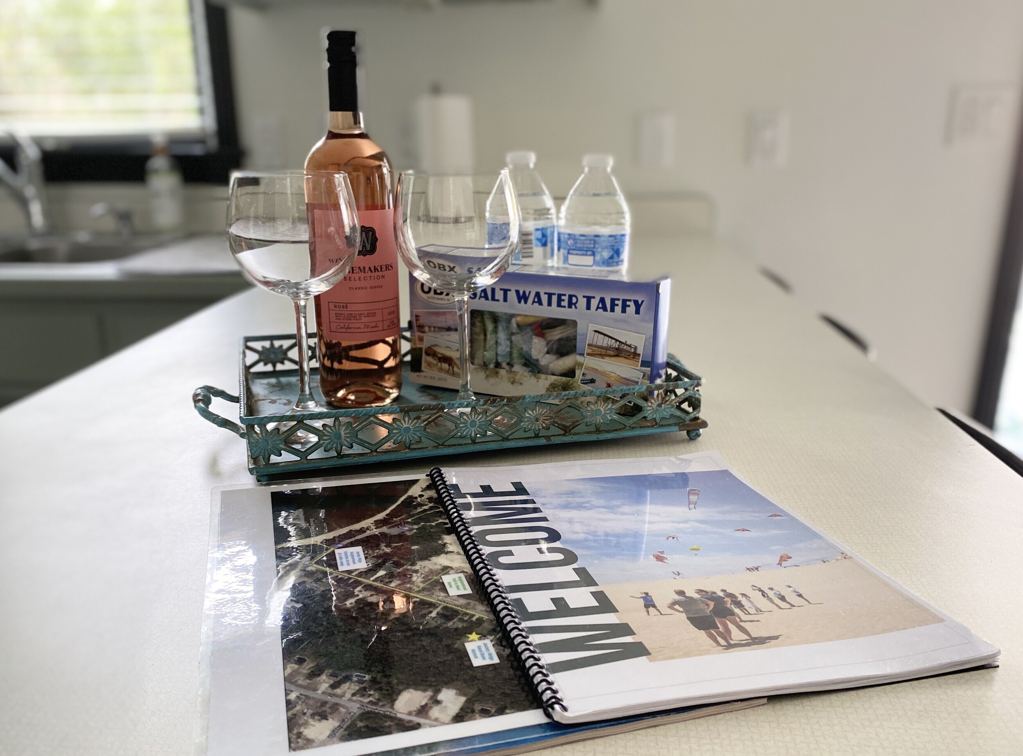 Una mesa con una bandeja decorativa que sostiene una botella de vino, copas y botellas de agua. También se aprecia un folleto de bienvenida sobre la mesa.