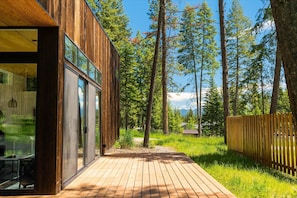 Un edificio moderno de madera con amplios ventanales, una terraza de madera y un paisaje boscoso de fondo.