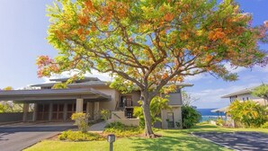 A two-story building with a covered entrance, a tree in front, and a clear view of the ocean.