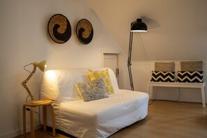 A white sofa with patterned cushions, a small wooden side table with a lamp, and a bench with woven cushions. - Comfortable apartment with river view and AC, fully equipped, very close to the center of Lisbon in the traditional Alfama district. (Lisboa ciudad)