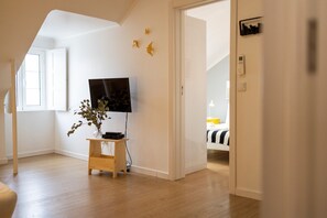 A room with a wooden floor, a TV on a stand, a plant, and a bed with a striped bedspread.