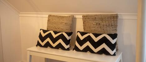A white bench with two black and white chevron pillows and two textured beige pillows.