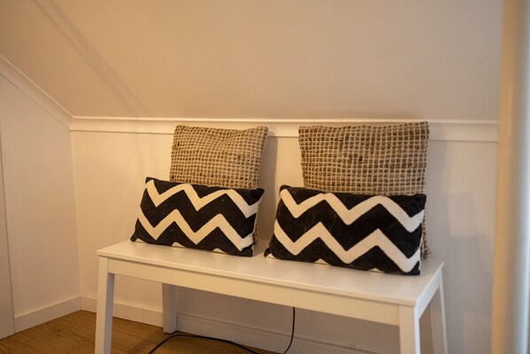 A white bench with two black and white chevron pillows and two textured beige pillows.