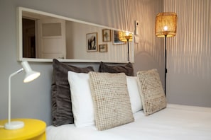 A bedroom with a bed, a mirror, a bedside lamp, and a floor lamp.