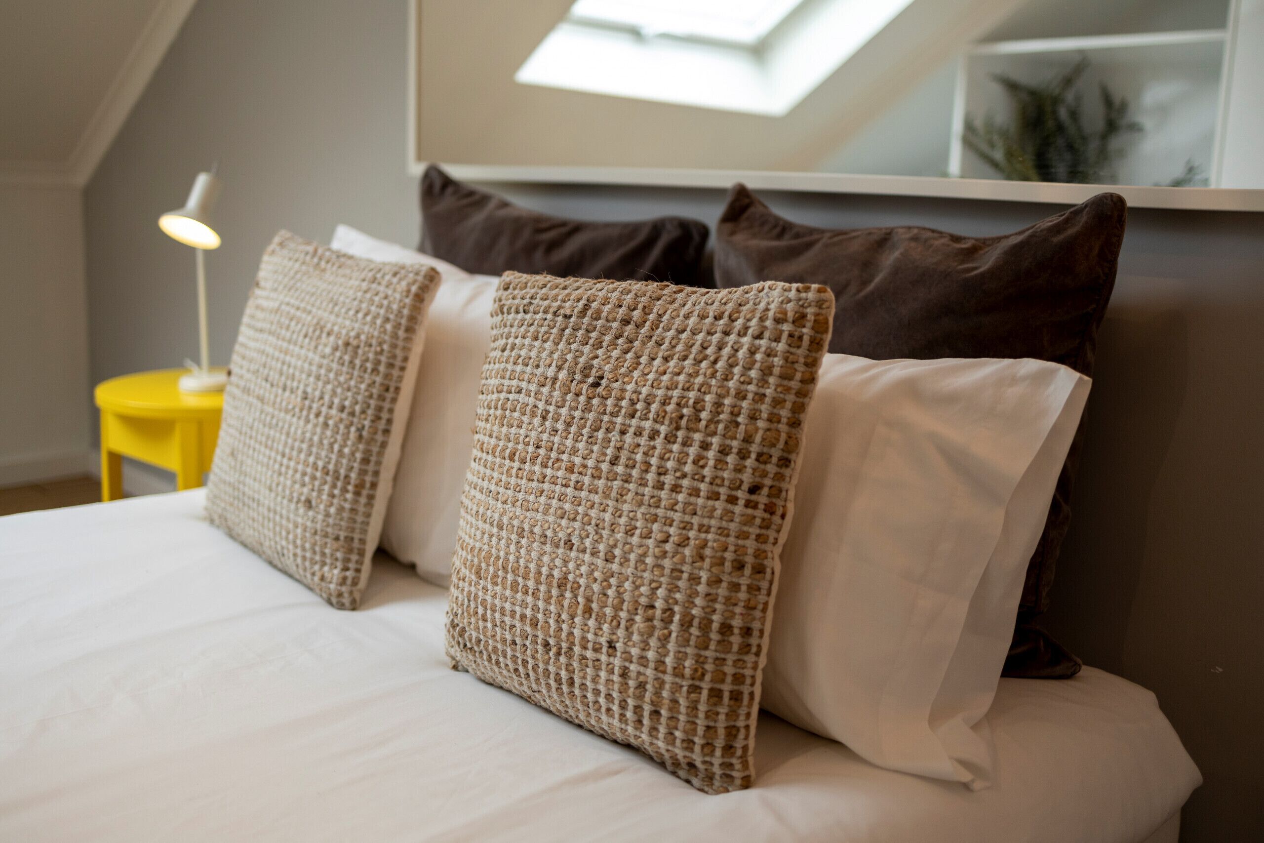 Een net opgemaakt bed met verschillende kussens en een bedlampje.