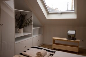 A bedroom with a skylight, a bed with a striped bedspread, a wooden nightstand, a white cabinet with shelves, and a potted plant. - Comfortable apartment with river view and AC, fully equipped, very close to the center of Lisbon in the traditional Alfama district. (Lisboa ciudad)