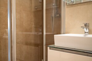 A bathroom with a glass shower enclosure, a white sink, and a mirror above the sink.