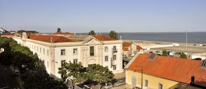 A coastal cityscape with a prominent white building with red-tiled roofs, a clear view of the sea, and a pedestrian crossing.