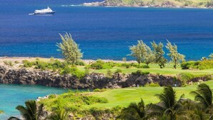 Une vue sur la côte, avec un terrain de golf, un navire sur l’océan et un paysage rocheux.