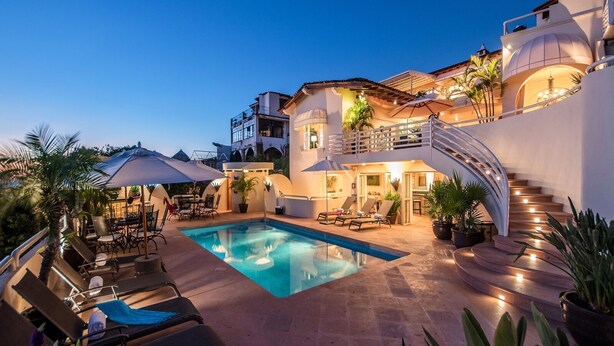 A pool area with lounge chairs and umbrellas, a staircase, and a building with balconies and plants.