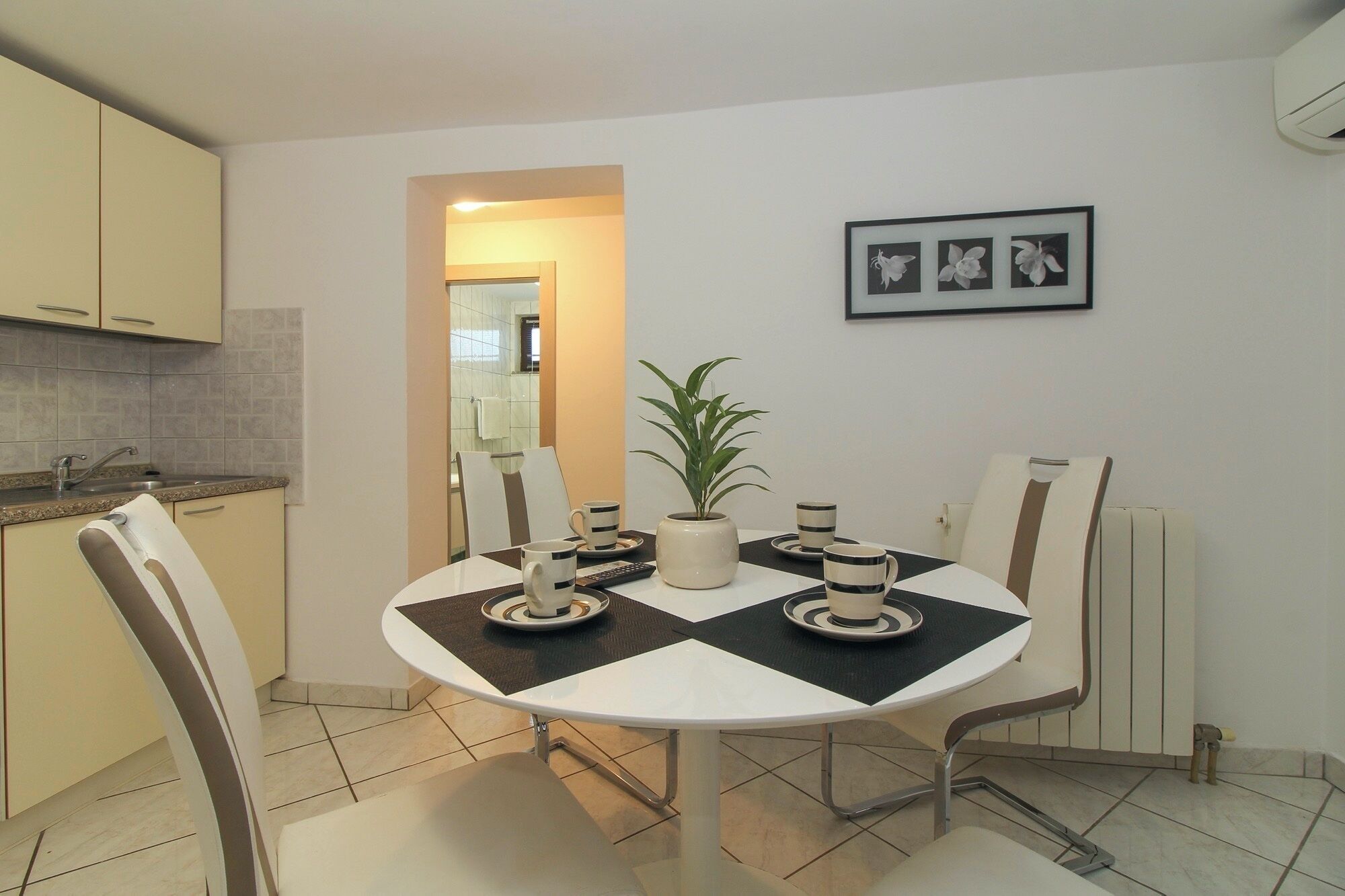 Une cuisine moderne avec un coin repas. Elle comprend une table ronde avec des chaises, une plante en pot et un tableau encadré accroché au mur.
