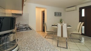 Cuina compacta amb fogó, rentapelats i zona menjador amb taula i cadires.