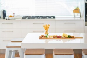 A modern kitchen with a white countertop, a wooden cutting board with food items, and a gas stove.