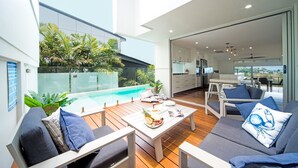 A modern outdoor living area with a pool, seating, and a view of the kitchen. - Oleander Holiday Home (Airlie Beach)