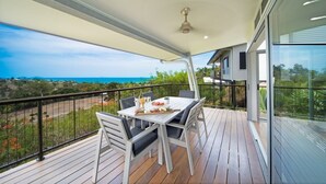 A balcony with a table set for dining, overlooking a coastal landscape. - Oleander Holiday Home (Airlie Beach)