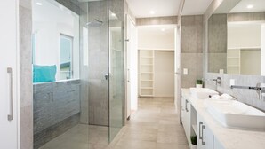 A modern bathroom with a glass-enclosed shower, a double sink vanity, and a large mirror. - Oleander Holiday Home (Airlie Beach)
