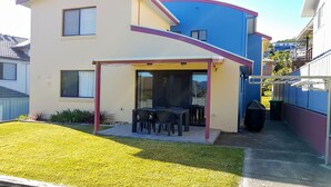 Ein zweistöckiges Haus mit einer überdachten Terrasse, auf der ein Tisch und Stühle stehen.