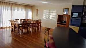 Ein Essbereich mit Holztisch und -stühlen, eine Küche mit schwarzem Kühlschrank und ein Fenster mit Jalousien.
