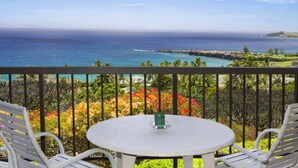 A balcony with a round table and two chairs, overlooking a coastal view with a clear sky. - Kapalua Ridge 2012- Whale Watching Ocean Views (Lahaina)