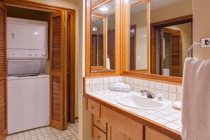 A bathroom with a white sink, mirror, wooden cabinets, and a built-in washing machine.