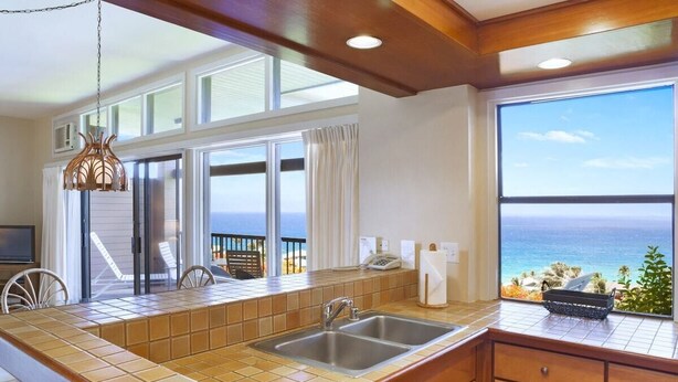 A kitchen with a large window overlooking the ocean, a sink, and a dining area with chairs. - Kapalua Ridge 2012- Whale Watching Ocean Views (Lahaina)
