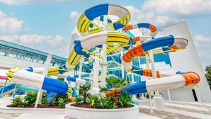 Un parc aquatique doté de nombreux toboggans et de plusieurs piscines, entouré de bâtiments et de palmiers.