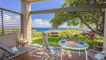 Une terrasse couverte avec vue sur l’océan, une table avec des chaises et un fauteuil de relaxation.
