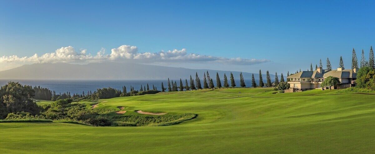 Un parcours de golf doté d’un club-house, offrant une vue dégagée sur l’océan et s’étendant devant un paysage montagneux.