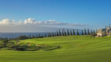 Un parcours de golf doté d’un club-house, offrant une vue dégagée sur l’océan et s’étendant devant un paysage montagneux.