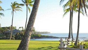 A golf course with a wooden fence, palm trees, and a view of the ocean. - Kapalua Ridge 411- Dazzling Ocean & Island Views! (Lahaina)
