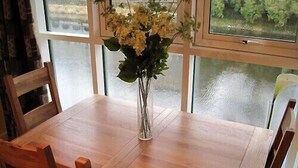 Un tavolo da pranzo in legno con sedie, un vaso con fiori e vista su un corpo d'acqua attraverso ampie finestre.