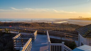 A wooden boardwalk leading to a beach with a dune and a building in the background.