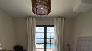 A bedroom with a large bed, a view of the sea through a window, and a wicker ceiling light. - French stonehouse with fantastic views (Théoule-sur-Mer)
