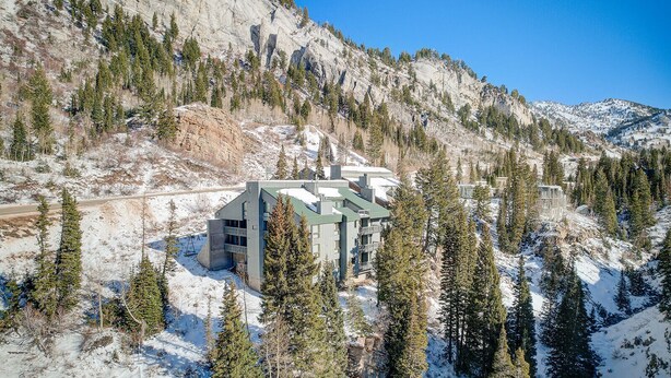 Un bâtiment moderne doté d’un toit végétalisé, entouré de montagnes enneigées et d’arbres à feuilles persistantes.